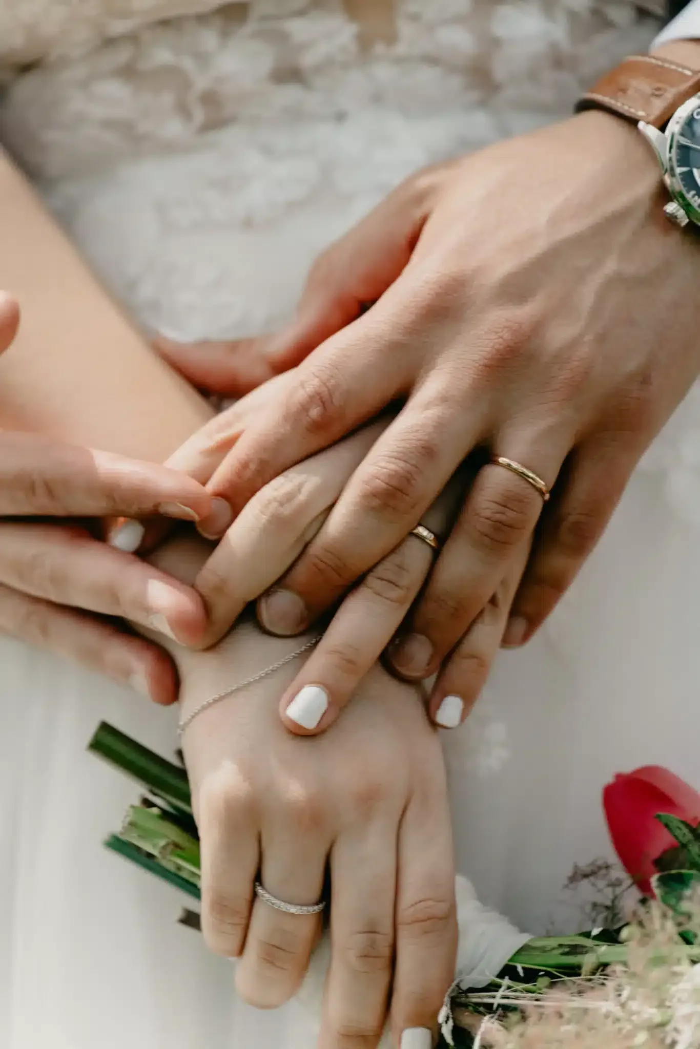 Las manos de los novios y sus alianzas junto al ramo